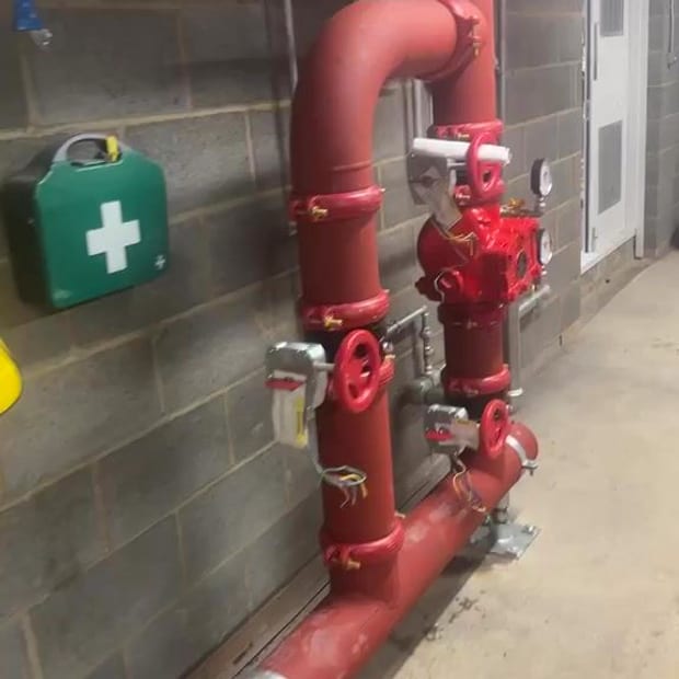 A new red wet alarm valve set and its pipework against a blockwork wall