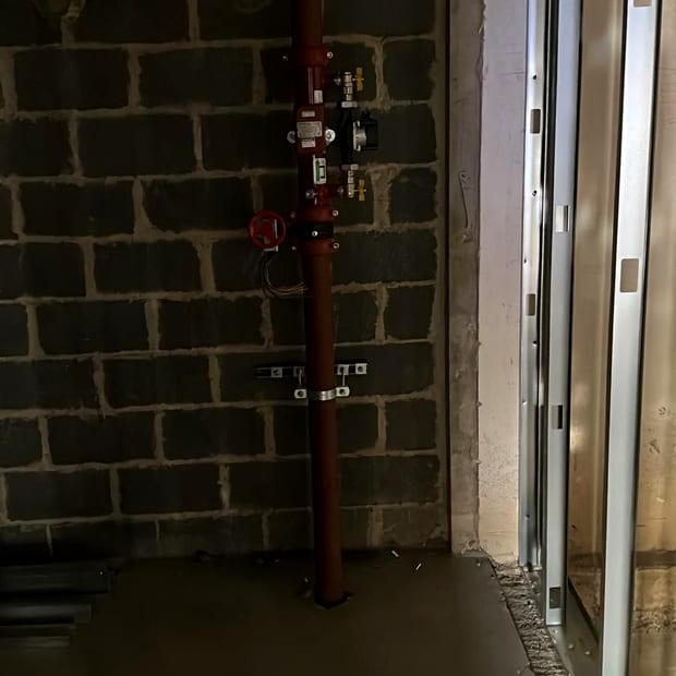A newly installed sprinkler zone control valve assembly on a red riser against a blockwork wall