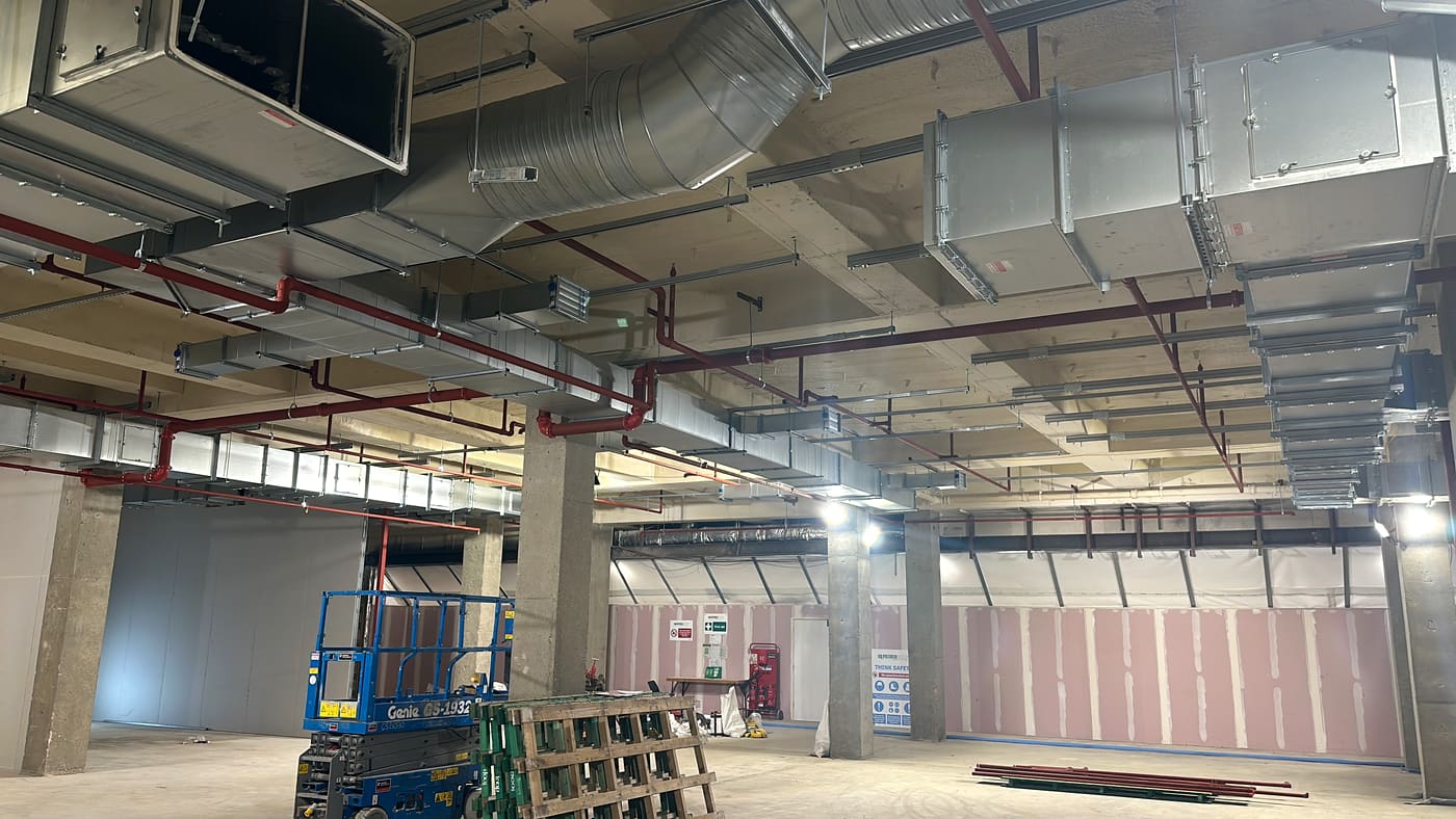 Red sprinkler mains and valve sets running through a commercial building under fit-out